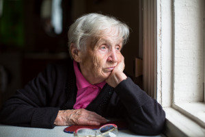 An elderly woman sadly looking out the window. Melancholy and de