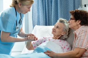 Doctor talking to elderly patient lying in bed in hospital